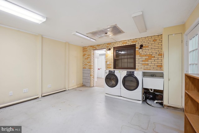 washroom featuring washer and dryer, laundry area, a sink, and brick wall