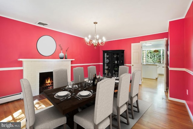 dining space featuring visible vents, a fireplace, wood finished floors, a baseboard heating unit, and an inviting chandelier