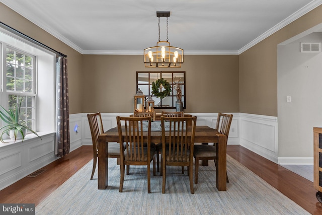 dining space with a chandelier, wood finished floors, visible vents, and crown molding