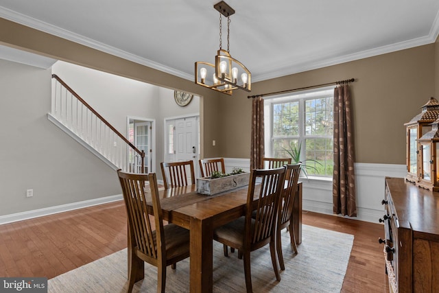 dining space featuring wainscoting, a notable chandelier, wood finished floors, stairs, and crown molding