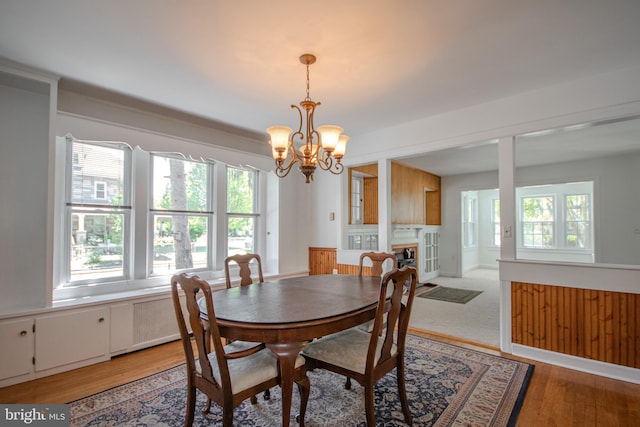 dining area featuring an inviting chandelier, a healthy amount of sunlight, light wood finished floors, and a fireplace
