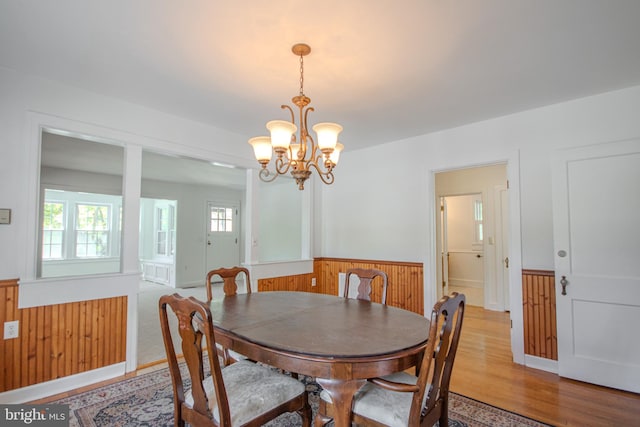 dining room with light wood-style floors, wainscoting, wood walls, and a notable chandelier