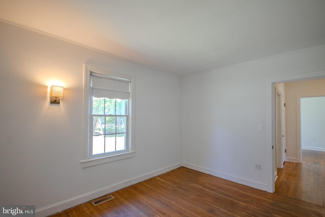 spare room featuring crown molding, baseboards, wood finished floors, and visible vents