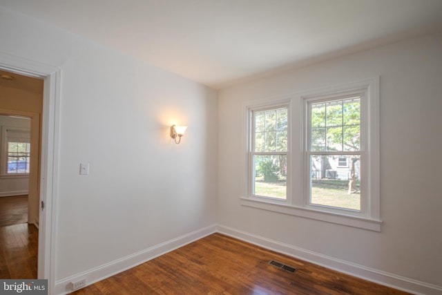 unfurnished room featuring baseboards, visible vents, dark wood-style floors, and a healthy amount of sunlight