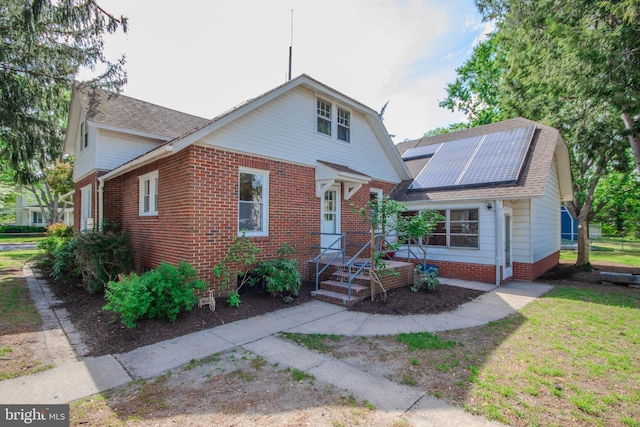bungalow-style house with brick siding, solar panels, and a shingled roof