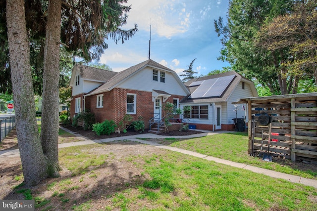 bungalow-style house featuring brick siding, fence, roof mounted solar panels, and a front lawn