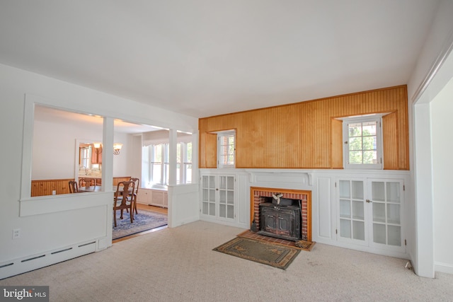 unfurnished living room featuring carpet floors, wooden walls, a baseboard heating unit, and a healthy amount of sunlight