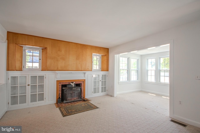unfurnished living room featuring plenty of natural light, a wood stove, carpet floors, and visible vents