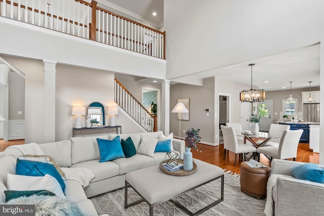 living area with decorative columns, a towering ceiling, stairs, light wood-style flooring, and a notable chandelier
