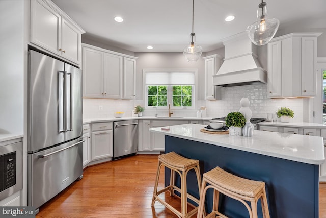 kitchen with a sink, a kitchen breakfast bar, light wood-style flooring, premium range hood, and stainless steel appliances