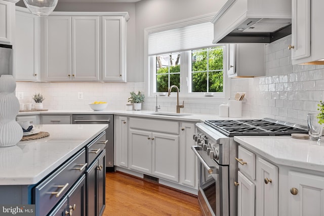 kitchen with white cabinets, appliances with stainless steel finishes, a sink, light wood-style floors, and custom range hood