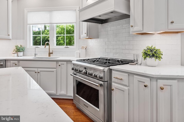 kitchen with white cabinets, a sink, stainless steel stove, and custom range hood