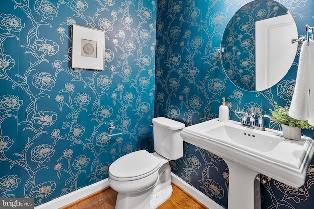 half bathroom with baseboards, toilet, wallpapered walls, and wood finished floors