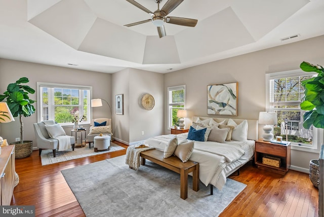 bedroom with wood-type flooring, a tray ceiling, visible vents, and baseboards