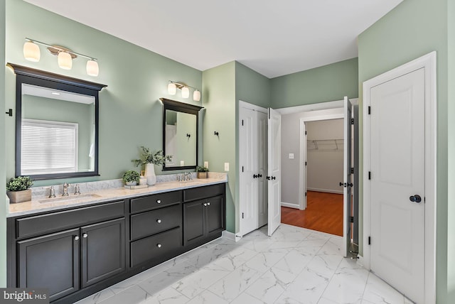 full bath with double vanity, a walk in closet, a sink, baseboards, and marble finish floor