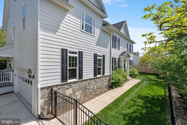 view of side of property with fence, a lawn, a garage, and stone siding
