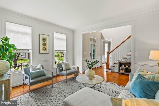 living area with ornamental molding, wood finished floors, and stairway