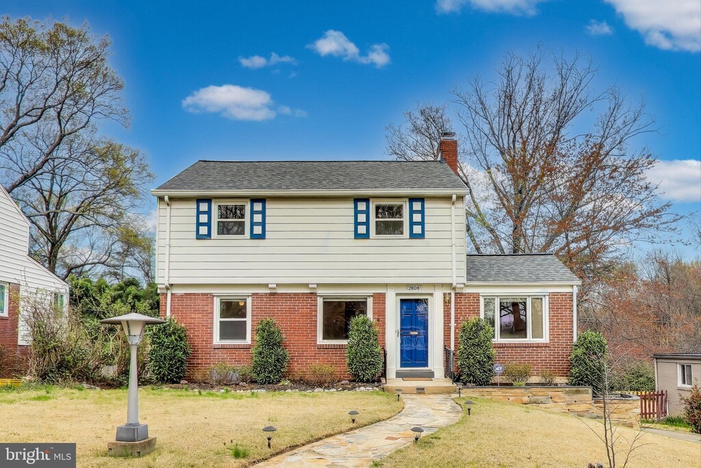 colonial home featuring brick siding, a front yard, roof with shingles, and a chimney