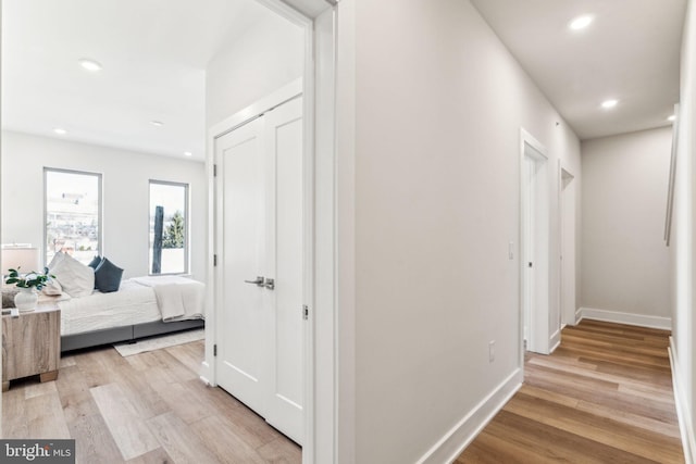 corridor featuring baseboards, light wood finished floors, and recessed lighting