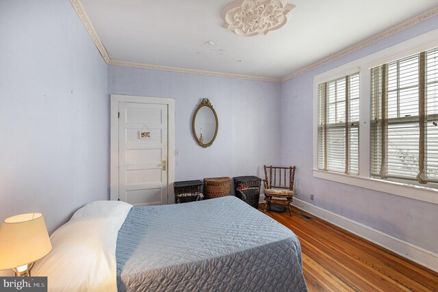 bedroom featuring baseboards, visible vents, crown molding, and wood finished floors