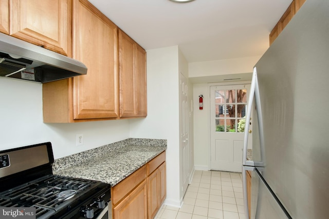 kitchen featuring light tile patterned floors, freestanding refrigerator, under cabinet range hood, stainless steel gas range oven, and light stone counters