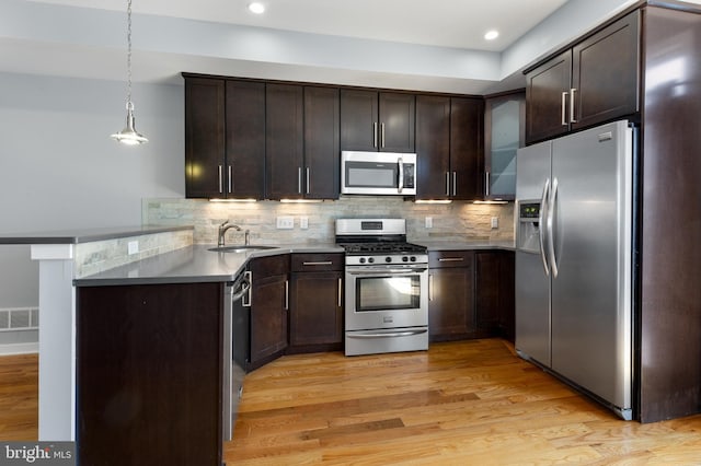 kitchen with a peninsula, light wood finished floors, stainless steel appliances, a sink, and backsplash