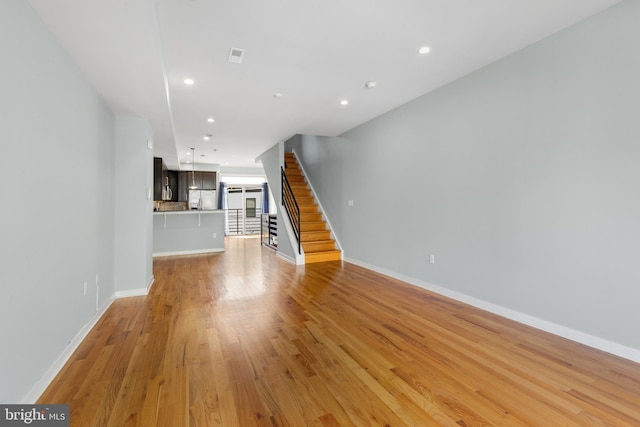 unfurnished living room with stairs, recessed lighting, light wood-style flooring, and baseboards