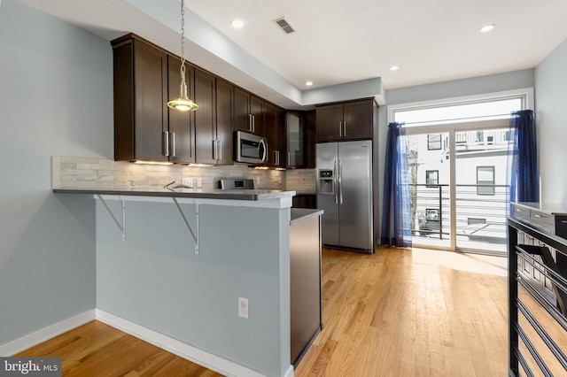 kitchen featuring tasteful backsplash, a kitchen bar, appliances with stainless steel finishes, visible vents, and dark brown cabinets