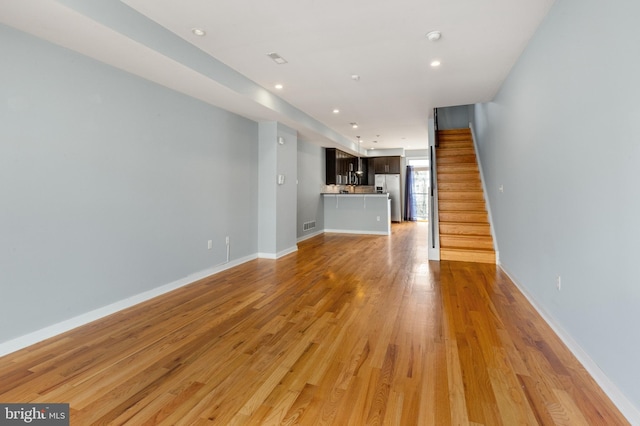 unfurnished living room with visible vents, light wood finished floors, baseboards, stairs, and recessed lighting