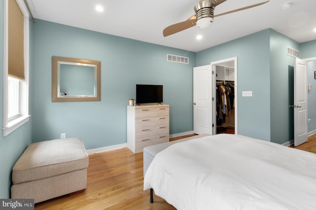 bedroom featuring a walk in closet, baseboards, light wood finished floors, and visible vents
