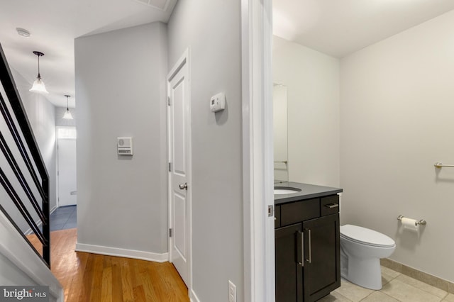 half bath with toilet, vanity, baseboards, and wood finished floors