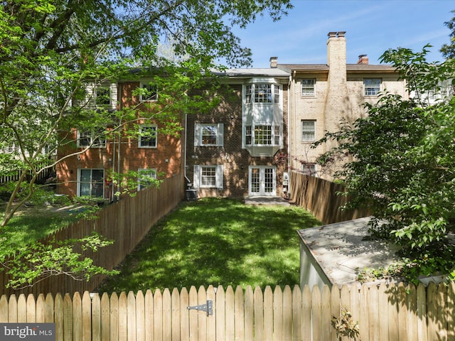 rear view of house featuring a fenced backyard, french doors, a chimney, brick siding, and a yard