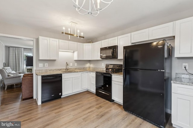 kitchen with a sink, a chandelier, light wood-style floors, black appliances, and light stone countertops