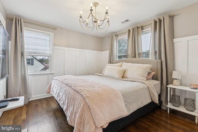 bedroom featuring a decorative wall, wood finished floors, a notable chandelier, and wainscoting
