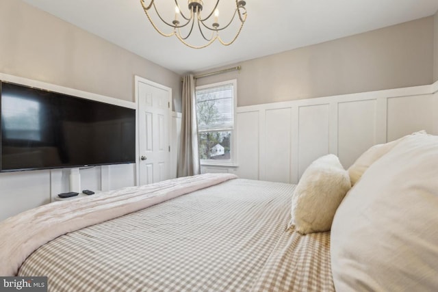 bedroom featuring a decorative wall, a notable chandelier, and wainscoting
