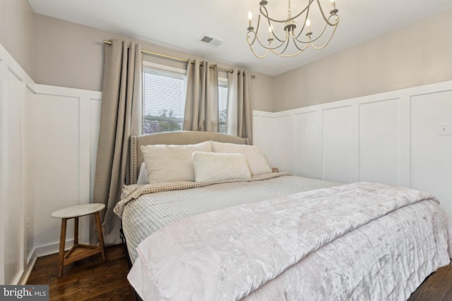 bedroom with a decorative wall, a notable chandelier, visible vents, and dark wood-style floors