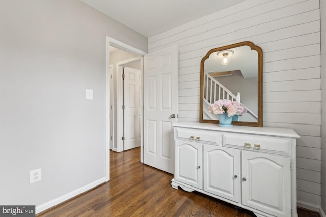 corridor with dark wood-type flooring, wood walls, and baseboards