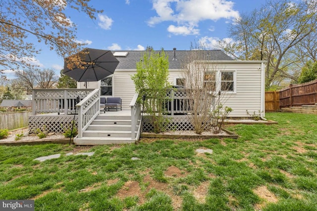 back of house with a shingled roof, a yard, a wooden deck, and fence