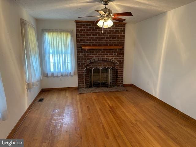 unfurnished living room featuring visible vents, baseboards, a ceiling fan, wood finished floors, and a brick fireplace