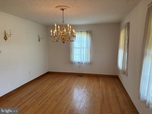 empty room featuring baseboards, wood finished floors, and a chandelier