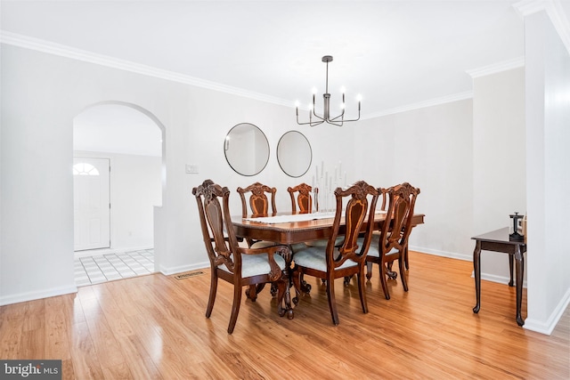 dining area featuring crown molding, visible vents, light wood-type flooring, a chandelier, and arched walkways