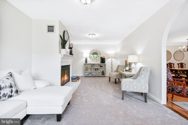 carpeted living area featuring visible vents, a glass covered fireplace, baseboards, a chandelier, and arched walkways