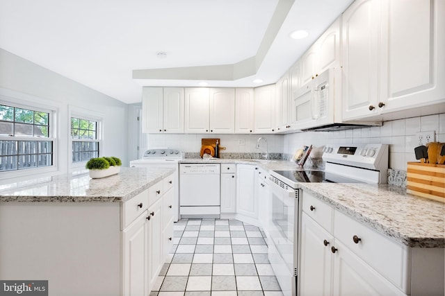 kitchen featuring tasteful backsplash, light stone countertops, white cabinets, washer / dryer, and white appliances