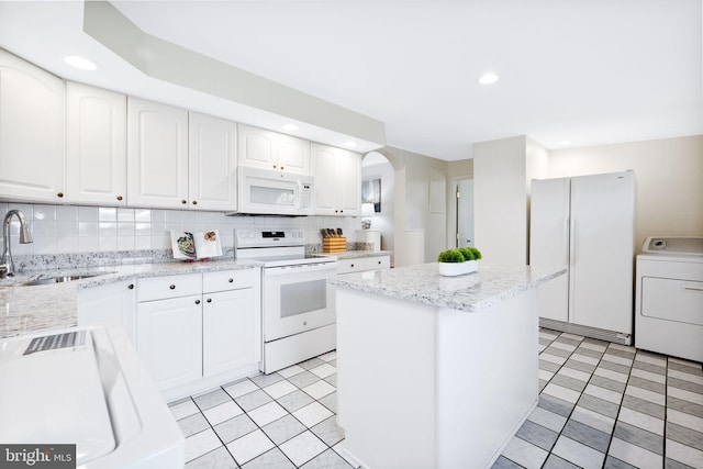 kitchen with a sink, white appliances, arched walkways, a center island, and washer / clothes dryer