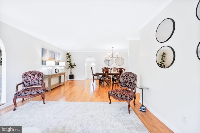 sitting room with arched walkways, wood finished floors, baseboards, a notable chandelier, and ornamental molding