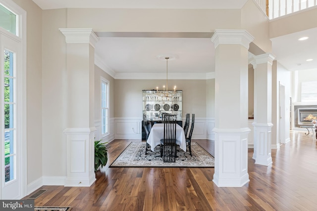 dining space with a wealth of natural light, a wainscoted wall, wood finished floors, and decorative columns