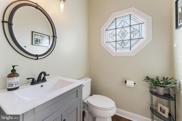 half bathroom with baseboards, toilet, and vanity
