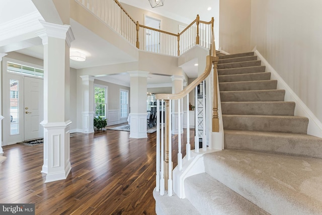 stairs featuring decorative columns, wood finished floors, a decorative wall, and crown molding