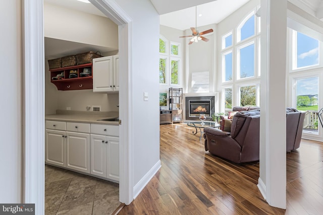 interior space with plenty of natural light, a ceiling fan, a high ceiling, and a glass covered fireplace