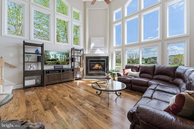 living area with a towering ceiling, a ceiling fan, a wealth of natural light, and hardwood / wood-style flooring